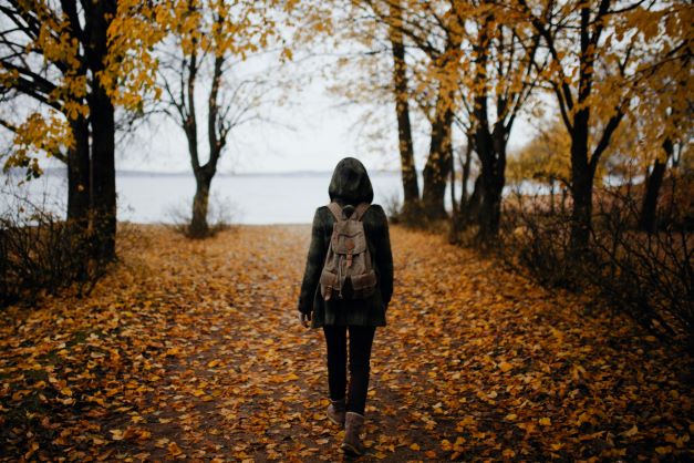 Žena je na procházce v parku během chladného podzimního dne. Listy jsou zbarvené do hněda.